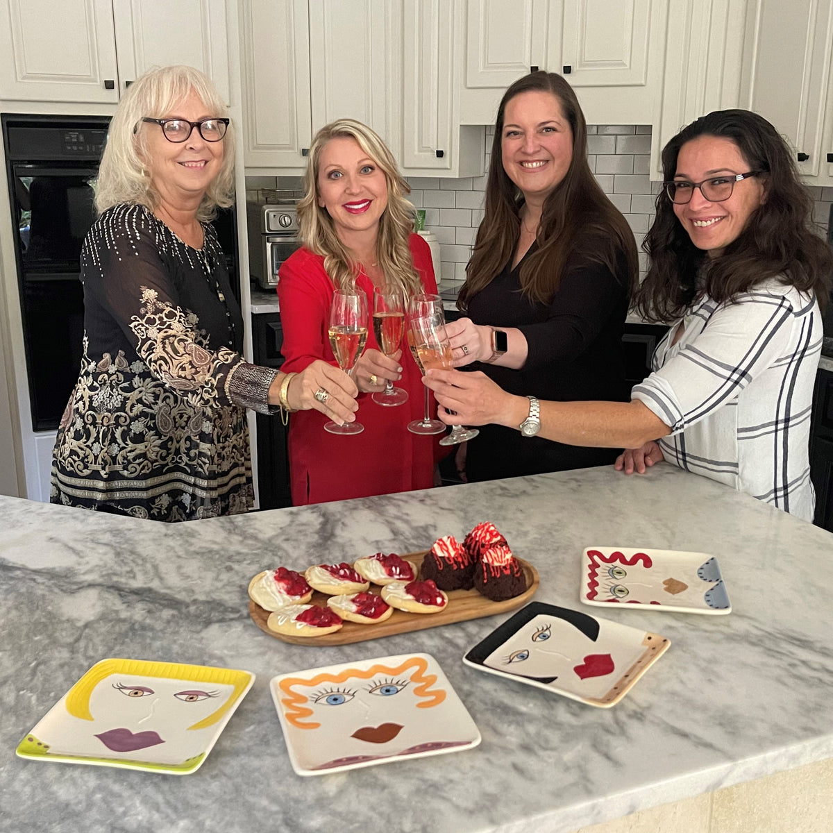 Four friends have a champagne toast over Personality Plates jut before they serve themselves a a treat on the dessert plates  and enjoy a girls night in.